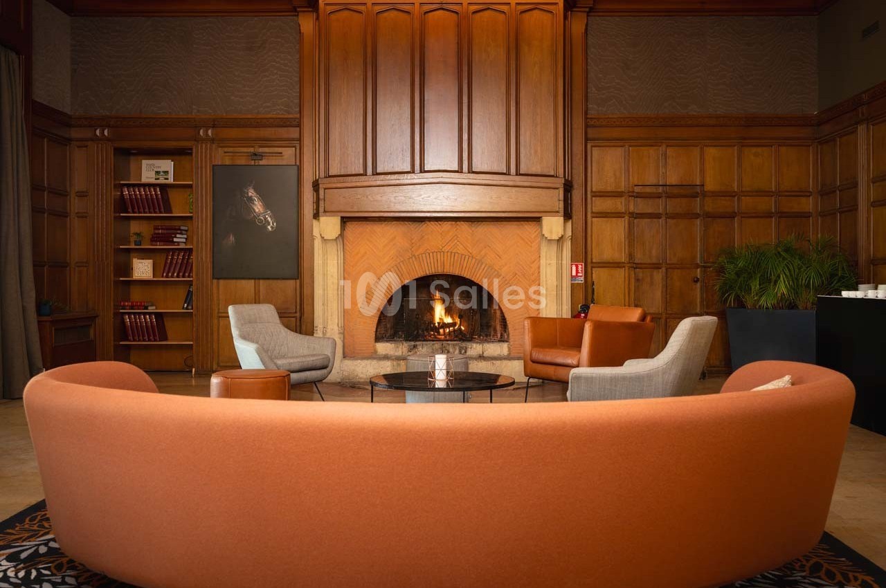 Salon chaleureux avec cheminée allumée, fauteuils modernes, bibliothèque et plantes dans un décor en bois.