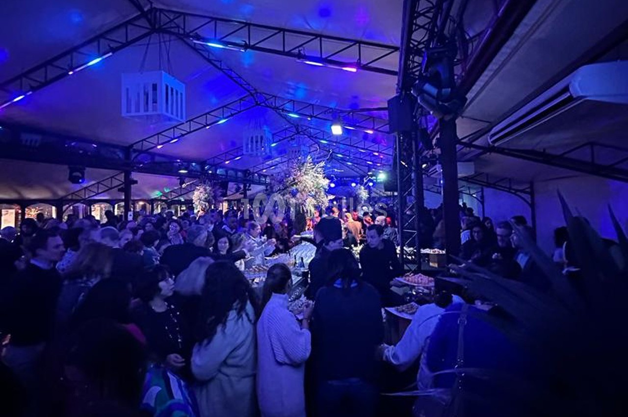Foule rassemblée dans un espace couvert illuminé de lumières bleues, autour de tables garnies de plats.
