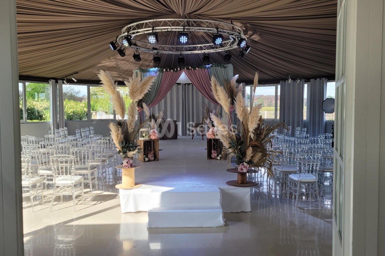 Salle de réception décorée avec des chaises transparentes, des arrangements floraux et un éclairage suspendu.