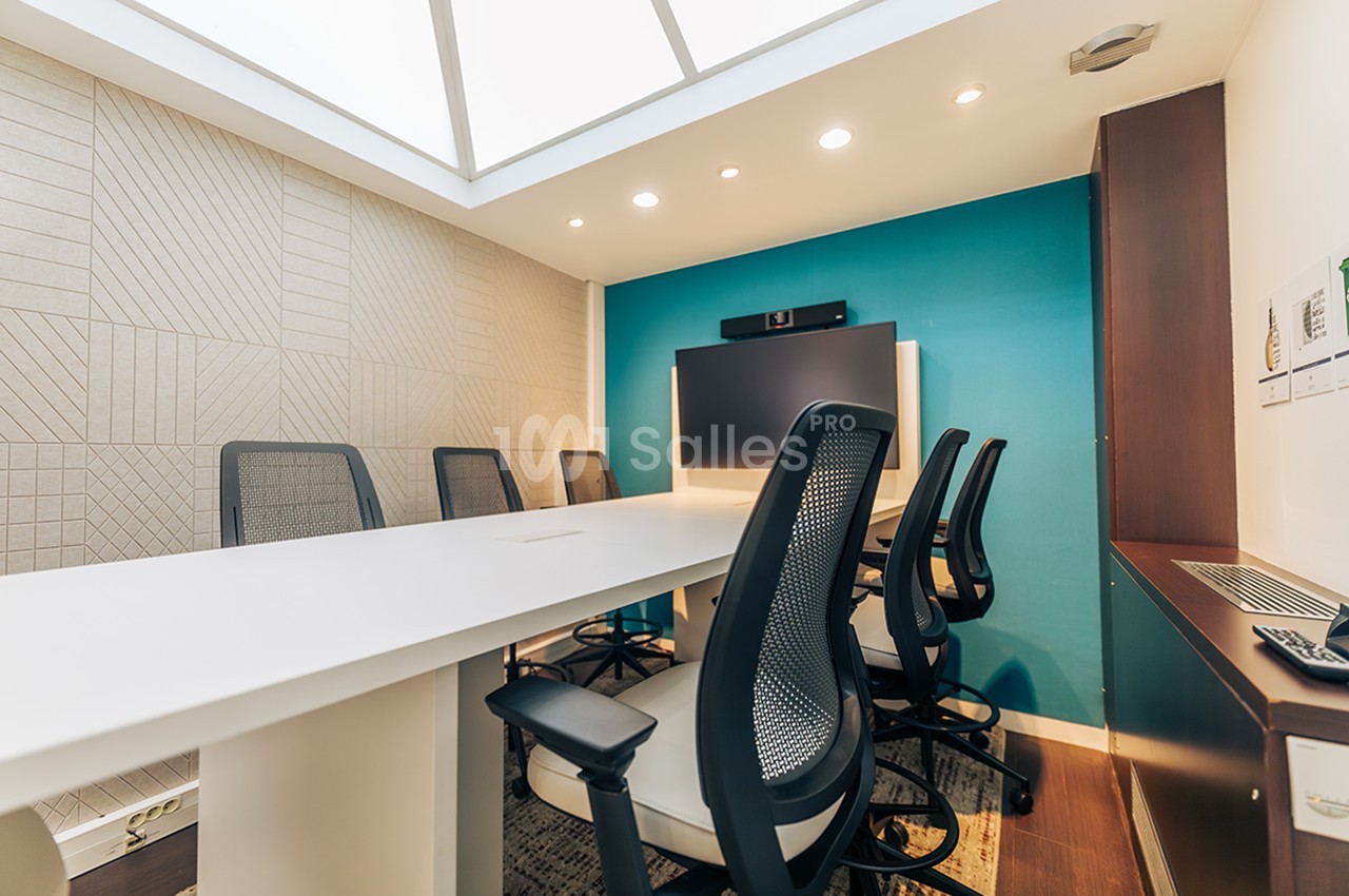 Salle de réunion moderne avec table blanche, chaises noires, mur bleu et éclairage intégré au plafond.