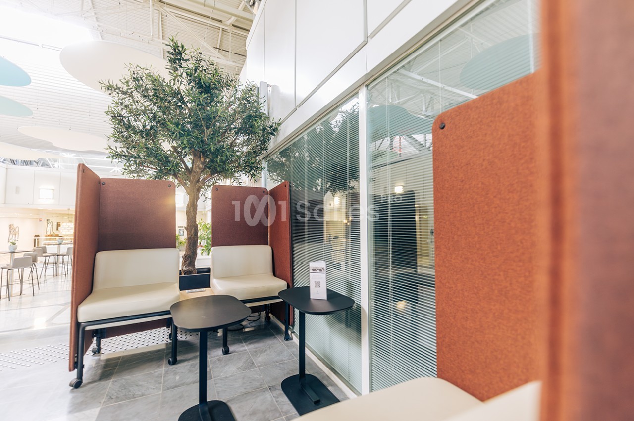 Espace de travail moderne avec sièges, tables noires, cloison en verre et arbre décoratif en intérieur lumineux.