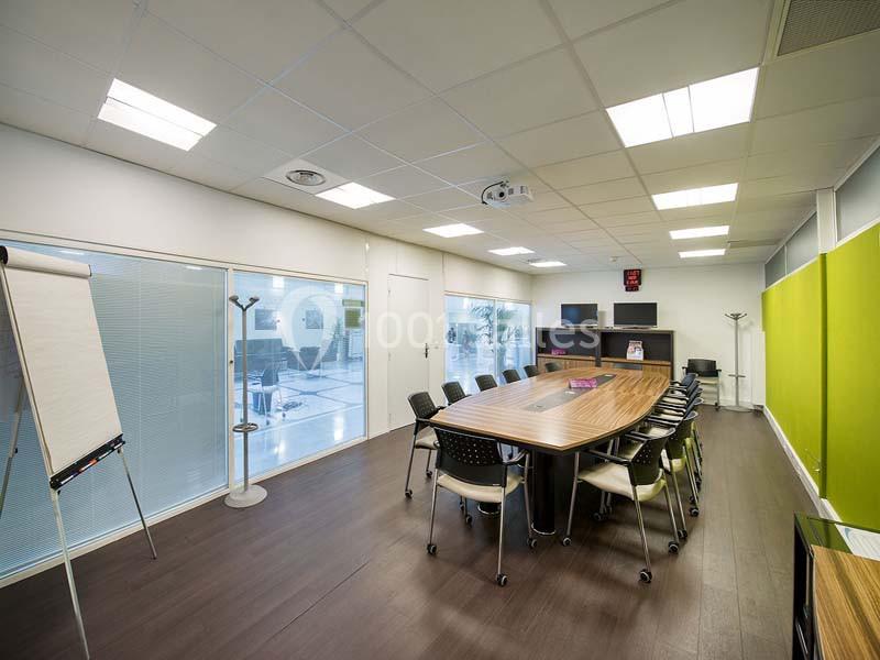 Salle de réunion lumineuse avec table en bois, chaises noires, tableau de conférence et équipements audiovisuels.