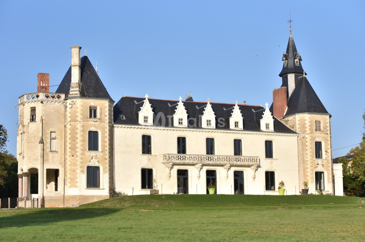 Façade d'un château de style néo-gothique avec tours et toit en ardoise, entouré d'une pelouse verdoyante.