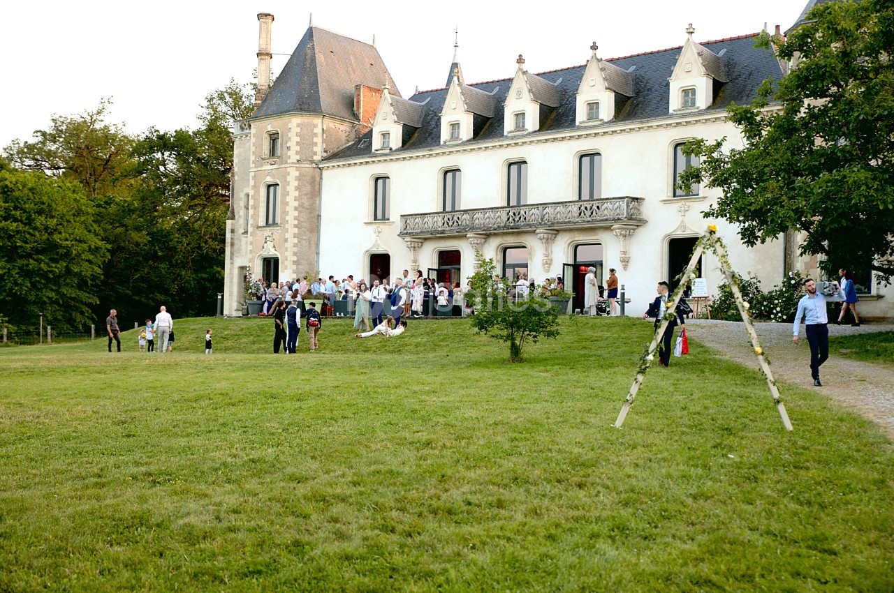 Groupe de personnes rassemblées devant un château entouré d'une pelouse et d'arbres.