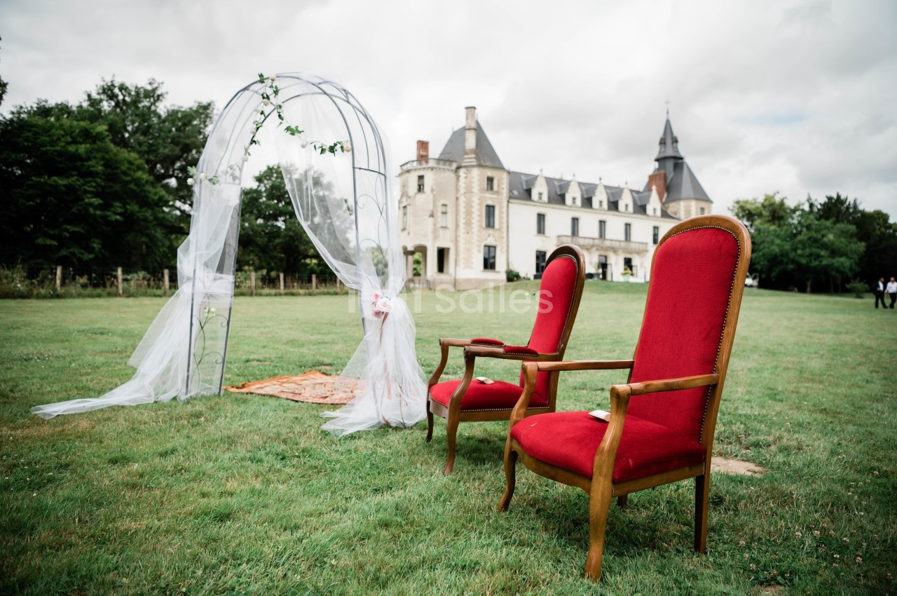 Deux fauteuils rouges disposés sur une pelouse devant une arche décorée et un château en arrière-plan.