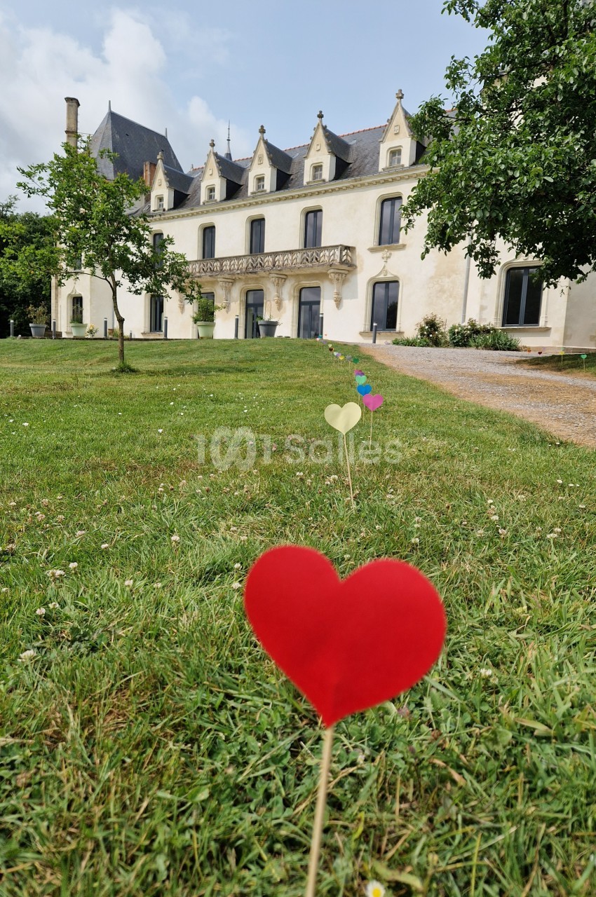 Cœurs en papier plantés dans une pelouse devant un grand bâtiment de style ancien entouré d'arbres.