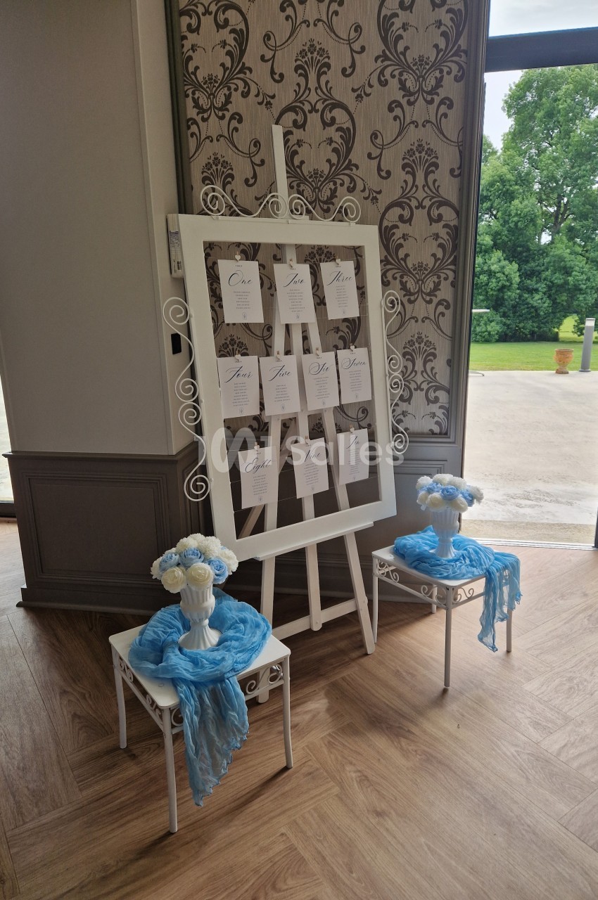 Un tableau d'affichage avec des cartes nominatives, entouré de décorations florales bleues, dans une salle lumineuse.
