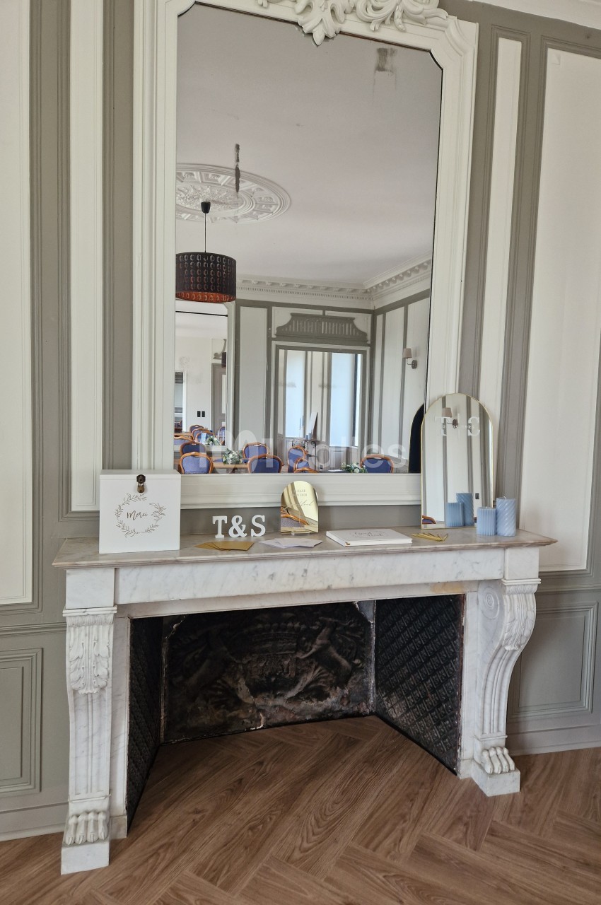 Cheminée décorative en marbre blanc surmontée d'un grand miroir, avec des objets posés sur le manteau.