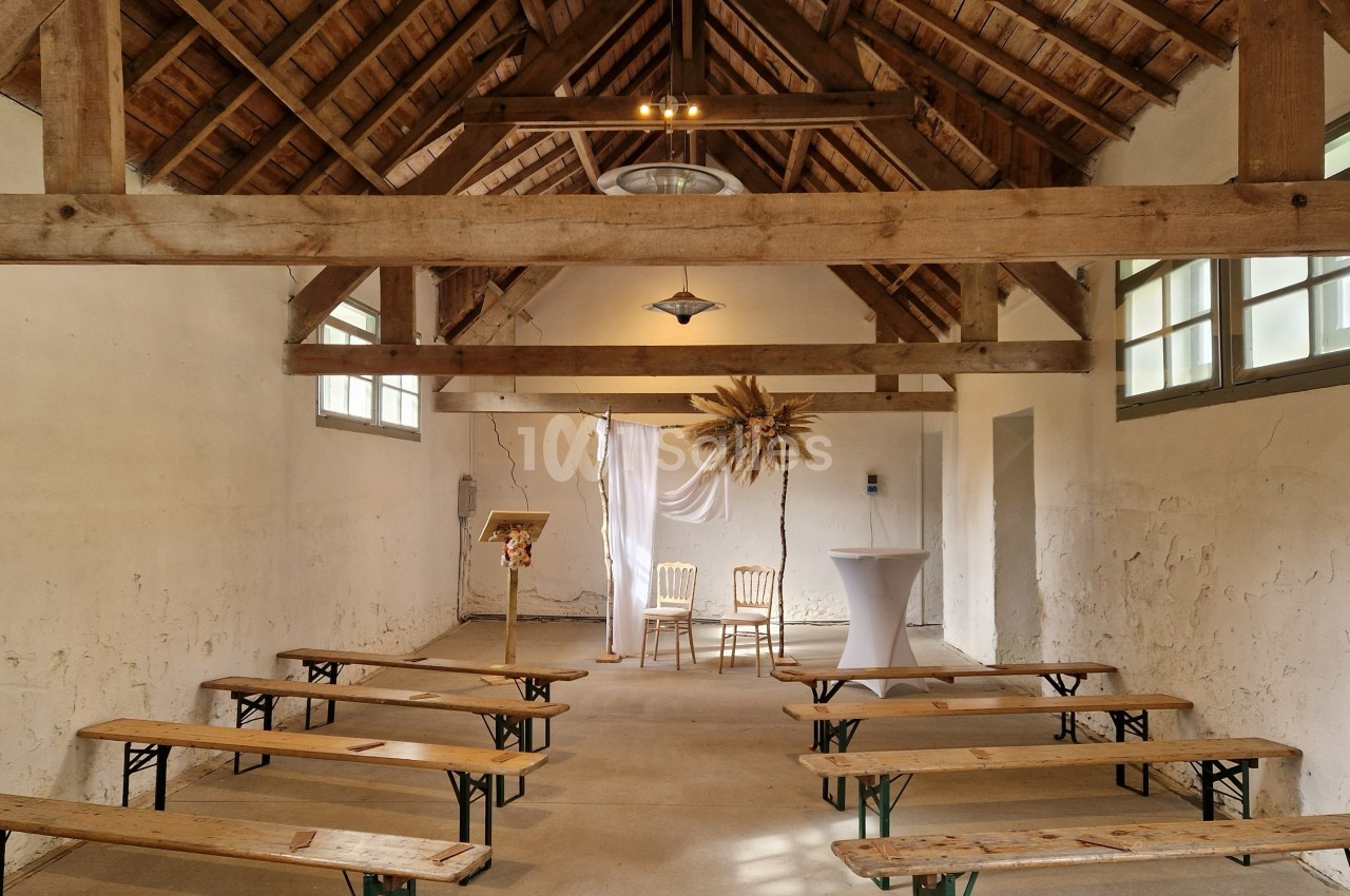 Intérieur d'une petite salle rustique avec bancs en bois, décorée pour une cérémonie avec deux chaises et un pupitre.