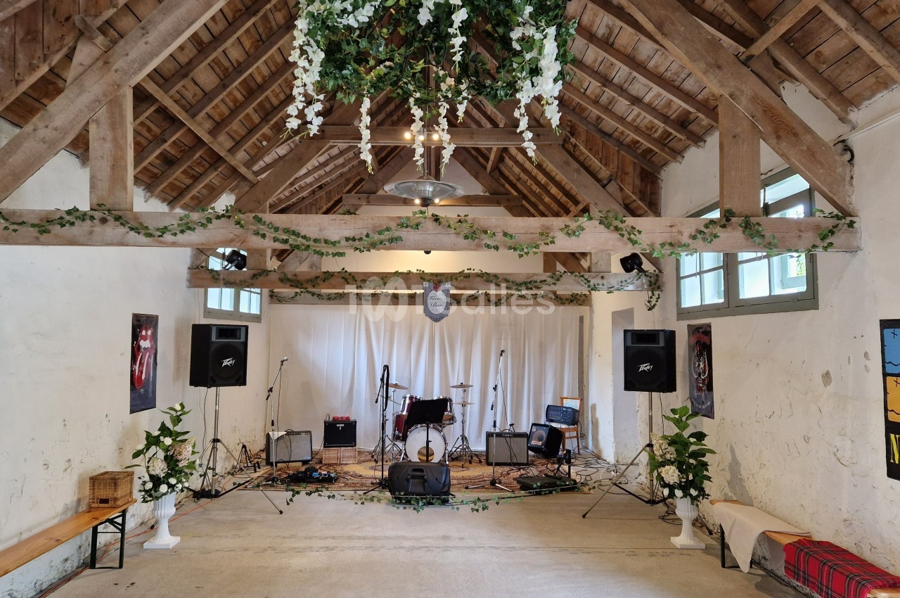 Salle rustique décorée de guirlandes végétales, avec une scène équipée d'instruments de musique et de matériel audio.