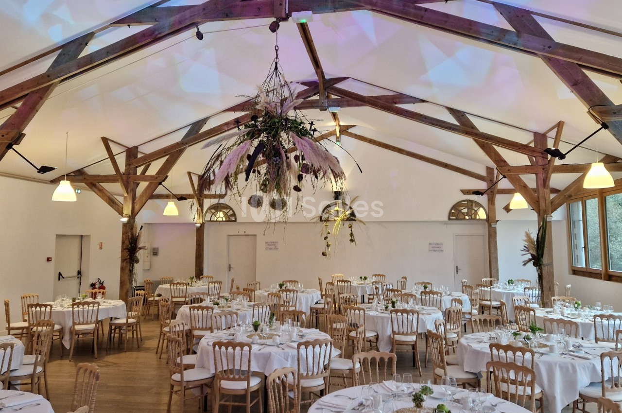 Salle de réception décorée avec des tables rondes dressées, des chaises en bois et une grande suspension florale.
