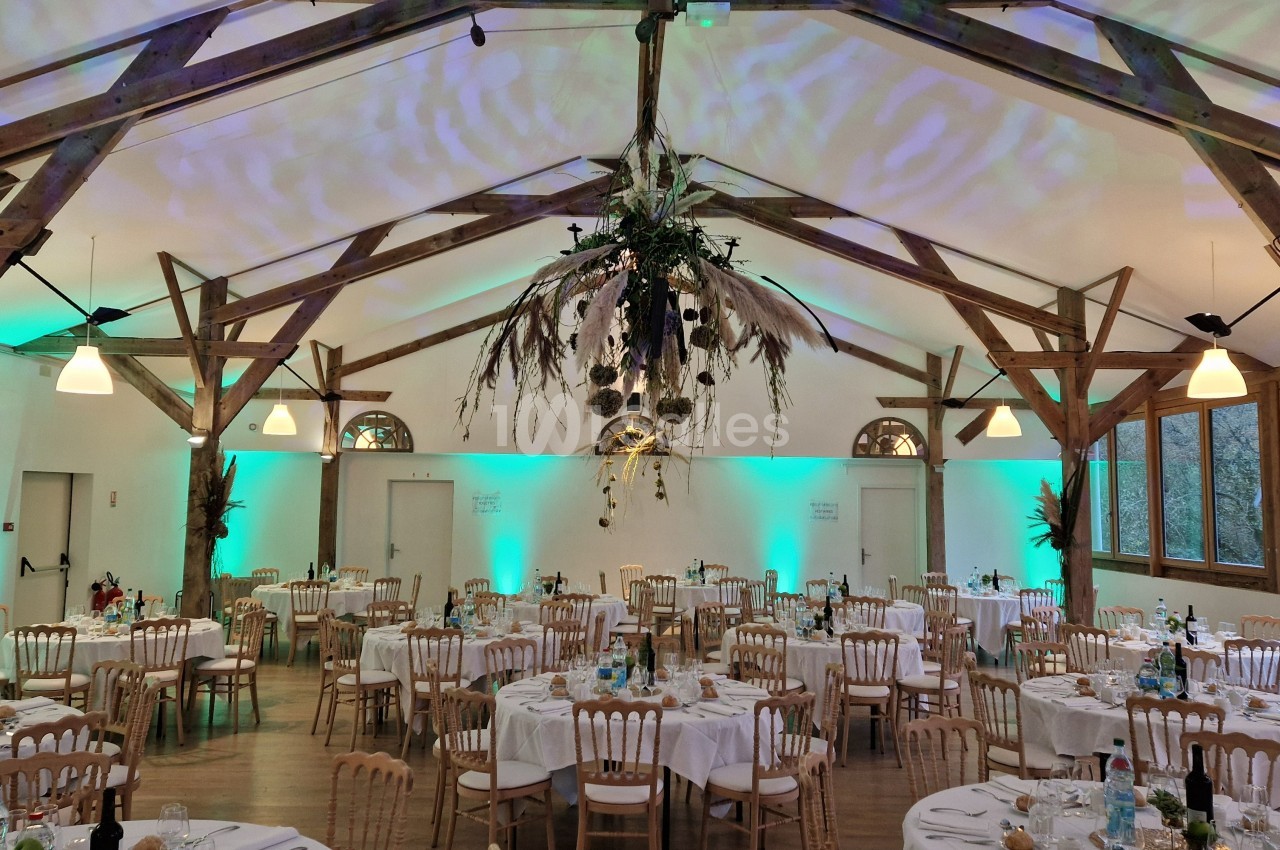 Salle de réception décorée avec des tables dressées, des chaises en bois et un éclairage tamisé aux tons verts.