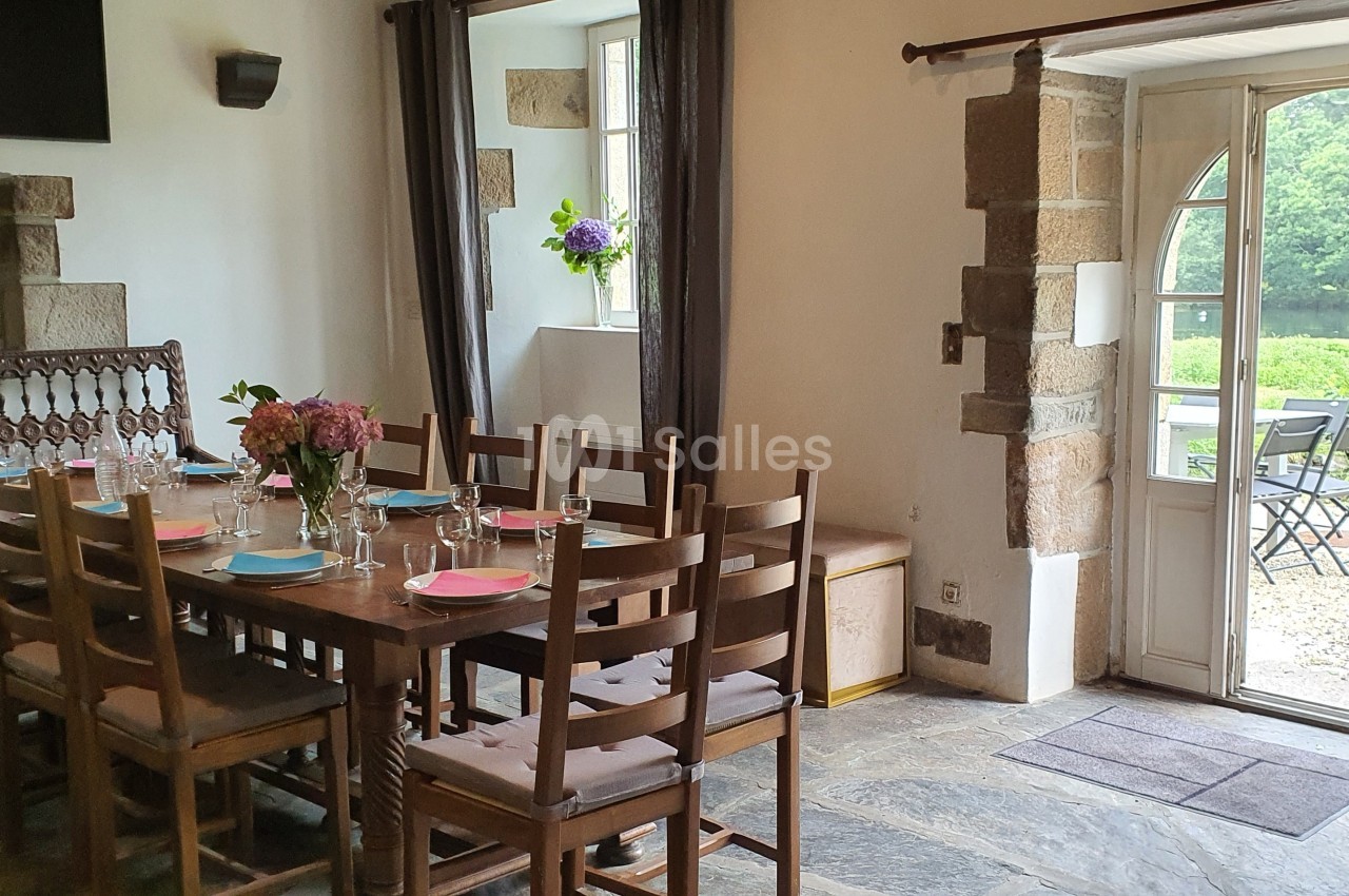 Salle à manger lumineuse avec une grande table en bois, des chaises assorties et une porte ouverte sur un jardin verdoyant.