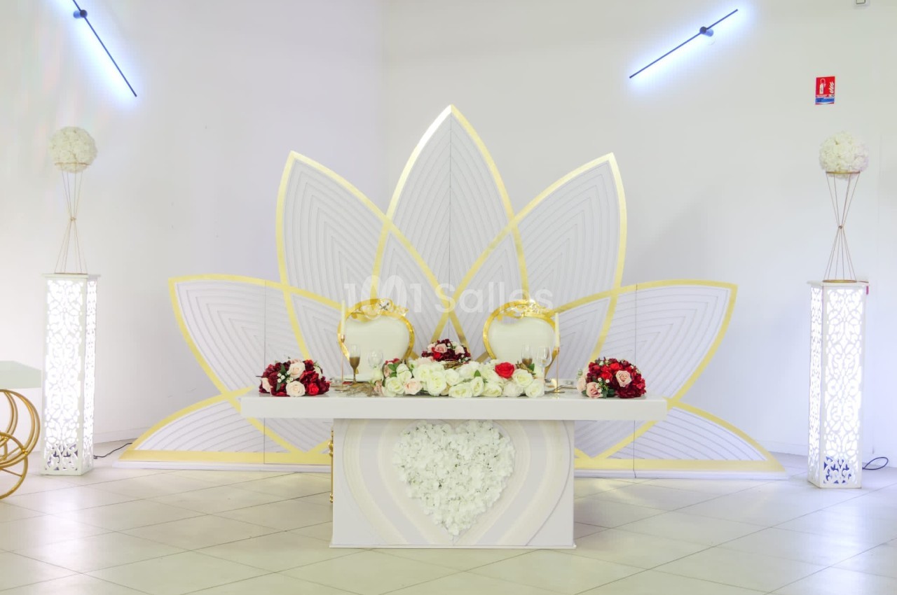 Table décorative de mariage avec fleurs rouges et blanches, chaises dorées et fond en forme de pétales dorés et blancs.
