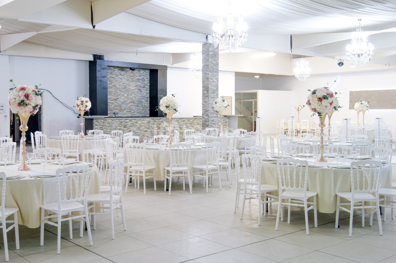 Salle de réception lumineuse avec tables rondes décorées de nappes blanches et centres de table fleuris.