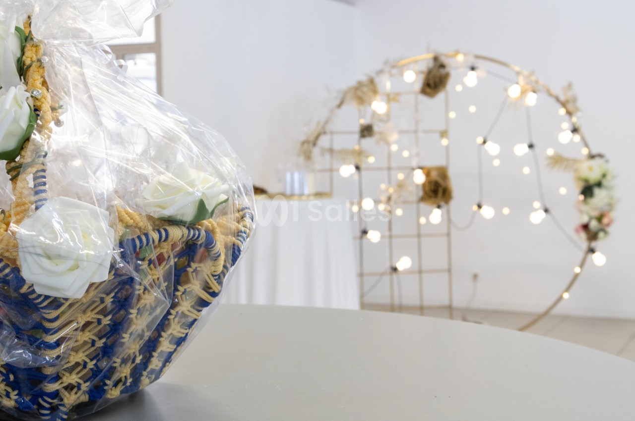 Panier décoratif avec des roses blanches en plastique, emballé dans un film transparent, devant une arche lumineuse.