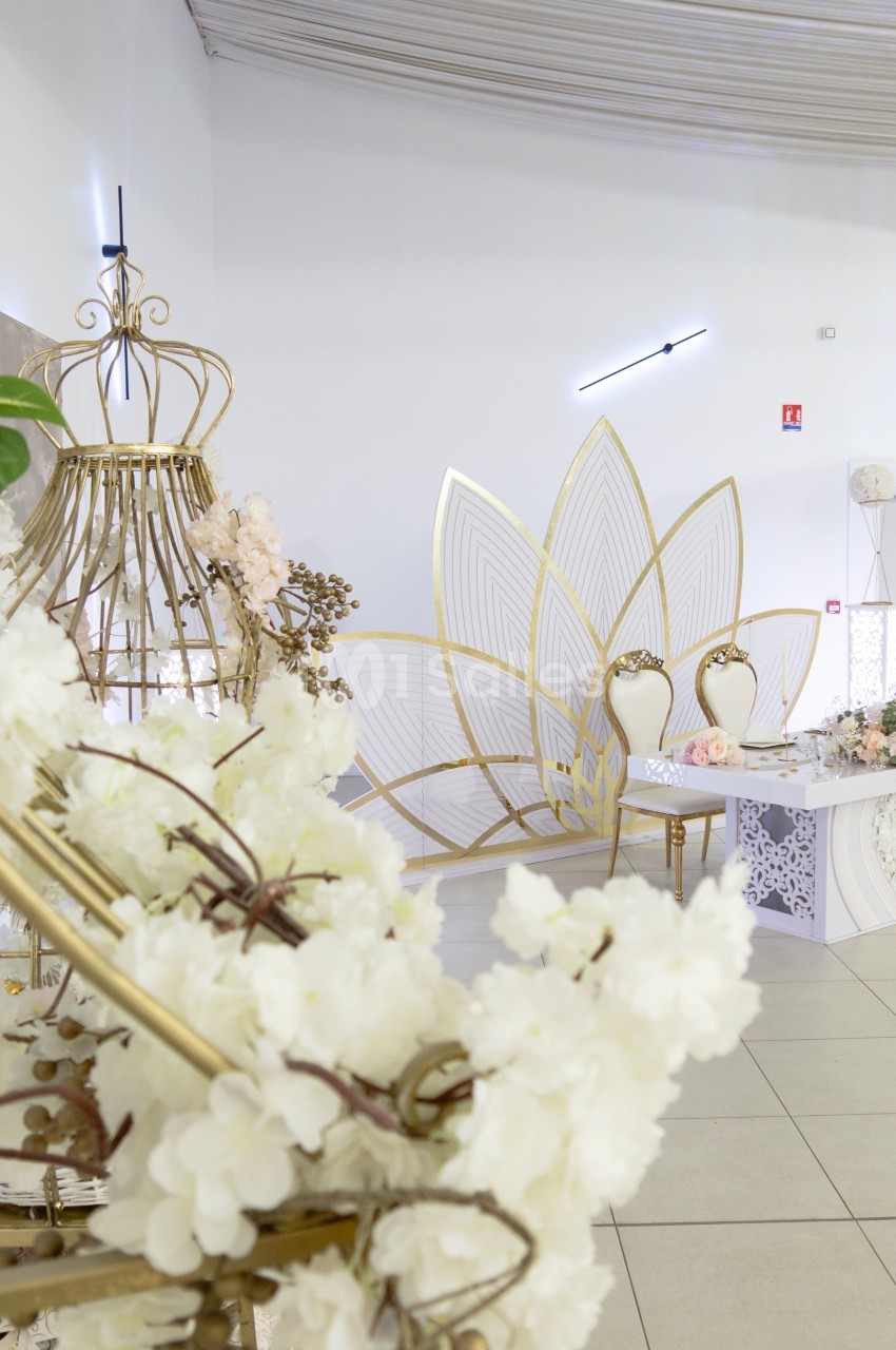 Décoration de salle avec fleurs blanches, chaises élégantes et structures dorées dans un espace lumineux.