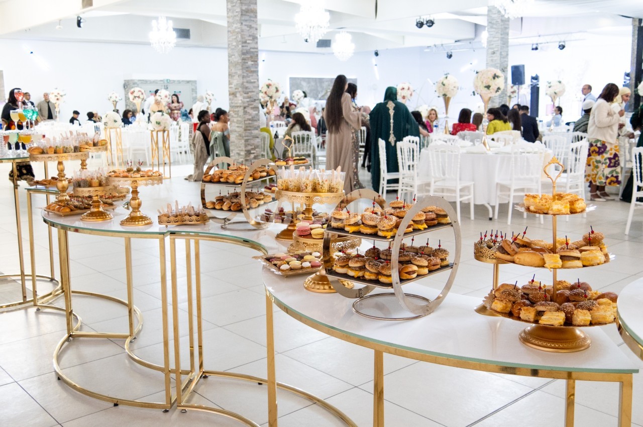 Buffet de desserts variés disposés sur des présentoirs dorés dans une salle de réception élégante.