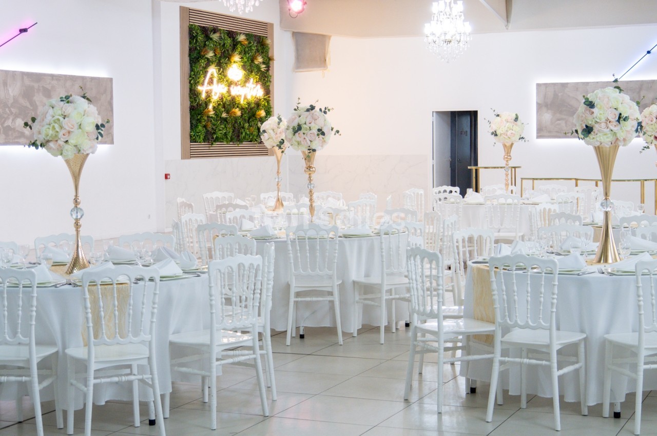 Salle de réception lumineuse avec tables rondes décorées de nappes blanches et centres de table fleuris.