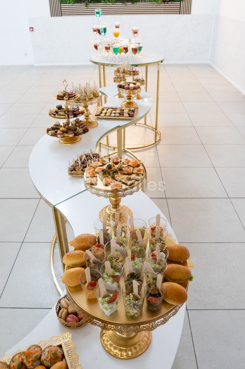 Buffet élégant avec une présentation variée de bouchées salées et sucrées sur des plateaux dorés en salle lumineuse.