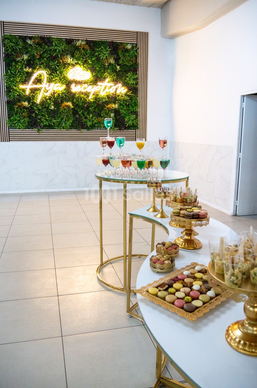 Buffet élégant avec desserts variés, cocktails colorés et mur végétal éclairé en arrière-plan.