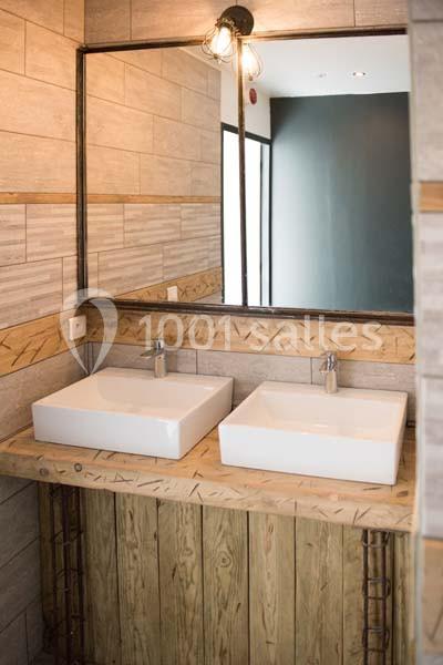 Deux lavabos rectangulaires blancs sur un meuble en bois, avec un grand miroir et un éclairage suspendu.