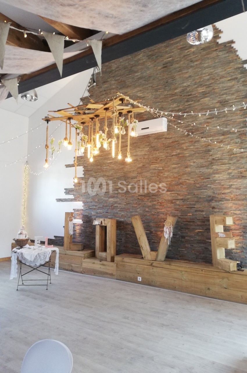 Décoration intérieure avec mur en pierre, guirlandes lumineuses suspendues et éléments en bois dans une salle lumineuse.