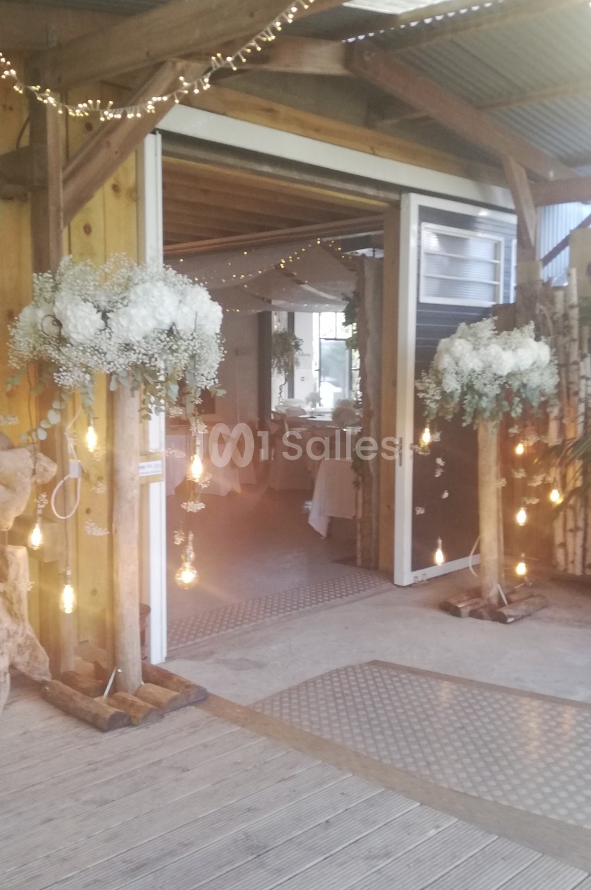Entrée décorée avec des guirlandes lumineuses, des fleurs blanches et des tables dressées visibles à l'intérieur.