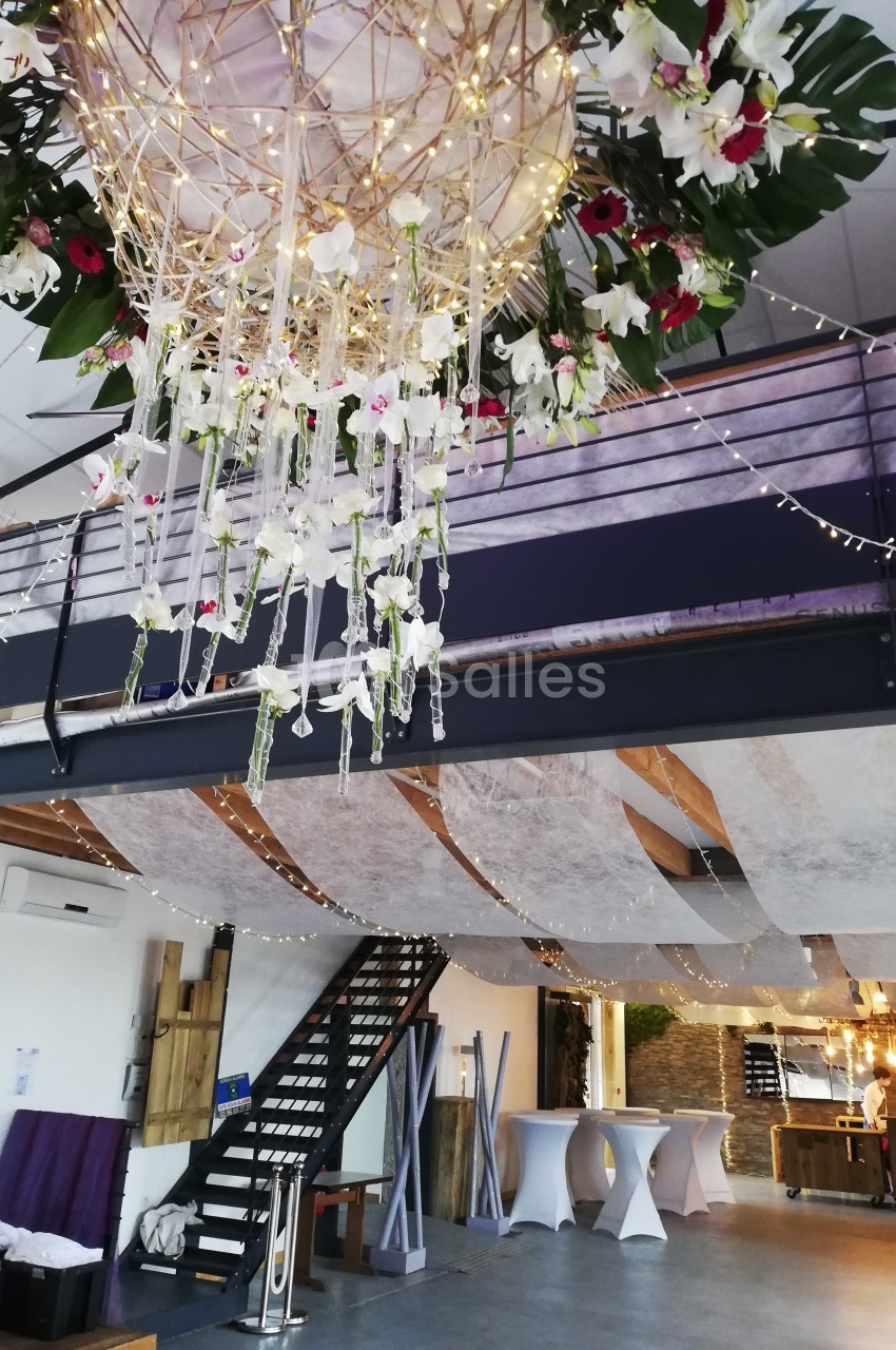 Décoration florale suspendue avec guirlandes lumineuses dans une salle de réception moderne à deux niveaux.