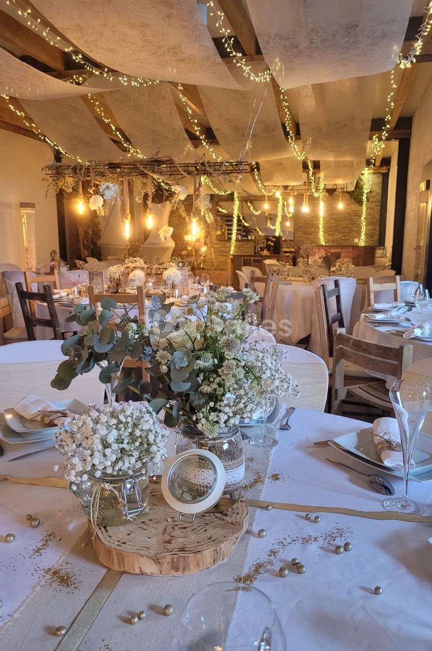 Salle de réception décorée pour un mariage avec tables dressées, guirlandes lumineuses et fleurs blanches.
