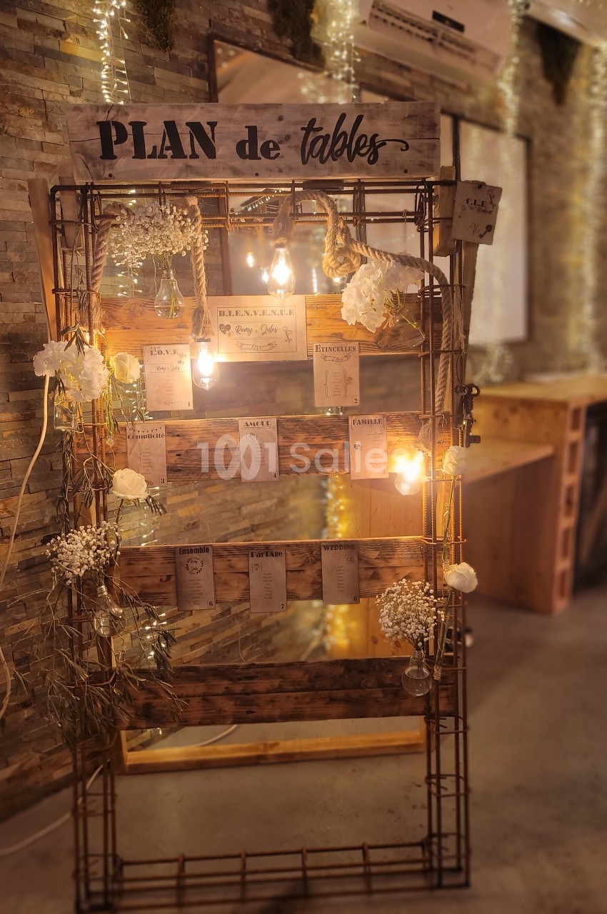 Plan de tables décoratif avec fleurs blanches, guirlandes lumineuses et cartes de placement suspendues sur une structure en…