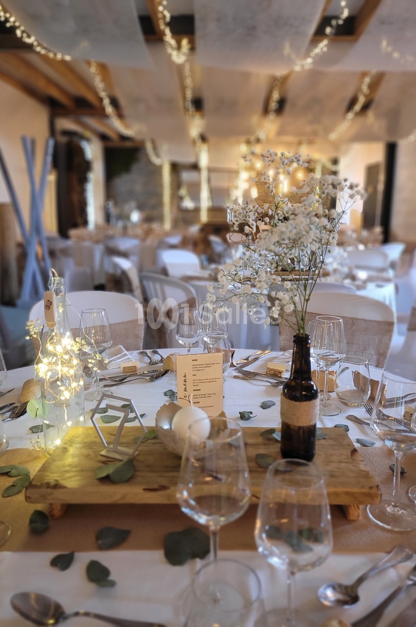 Salle de réception décorée pour un mariage, avec tables dressées, guirlandes lumineuses et centre de table floral.