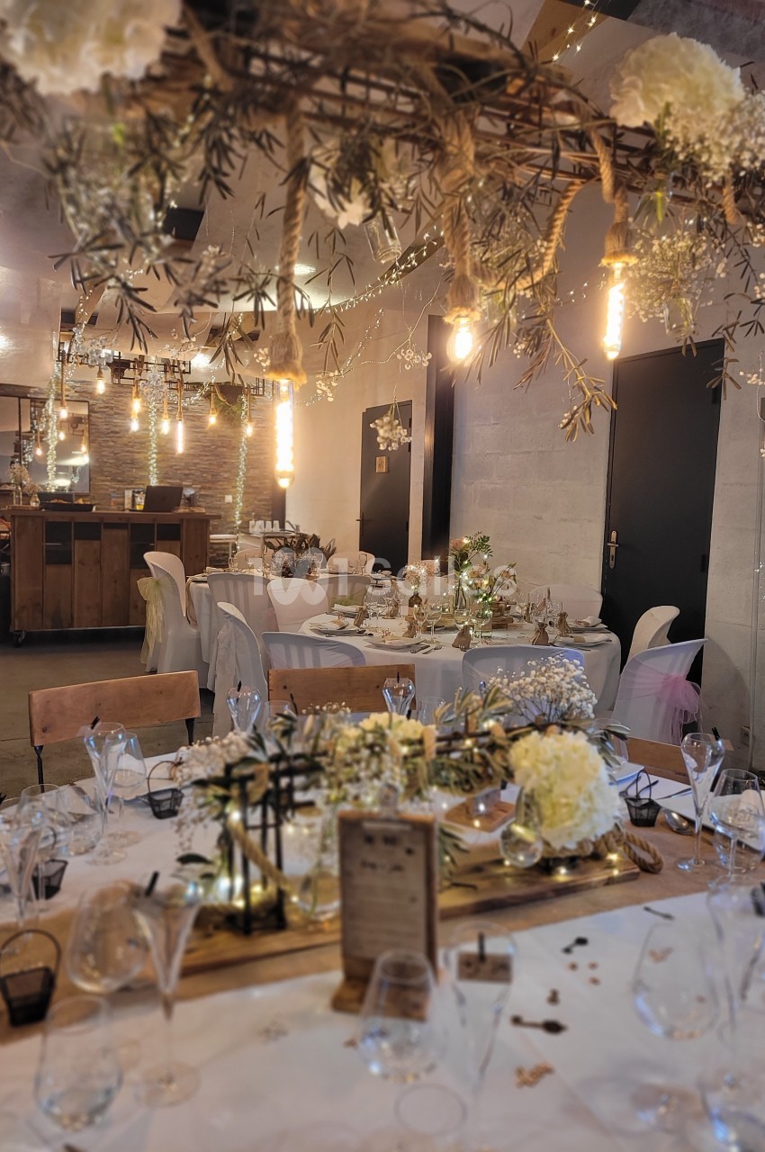 Salle de réception décorée avec des tables dressées, guirlandes lumineuses et ornements floraux suspendus.