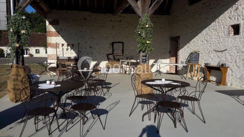 Terrasse couverte avec tables et chaises en fer forgé, décorée de sacs en toile et de guirlandes végétales.