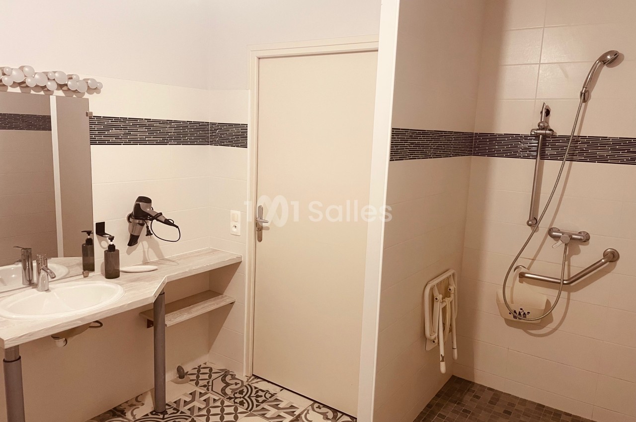 Salle de bain accessible avec douche à l'italienne, siège mural, barres d'appui et lavabo adapté.