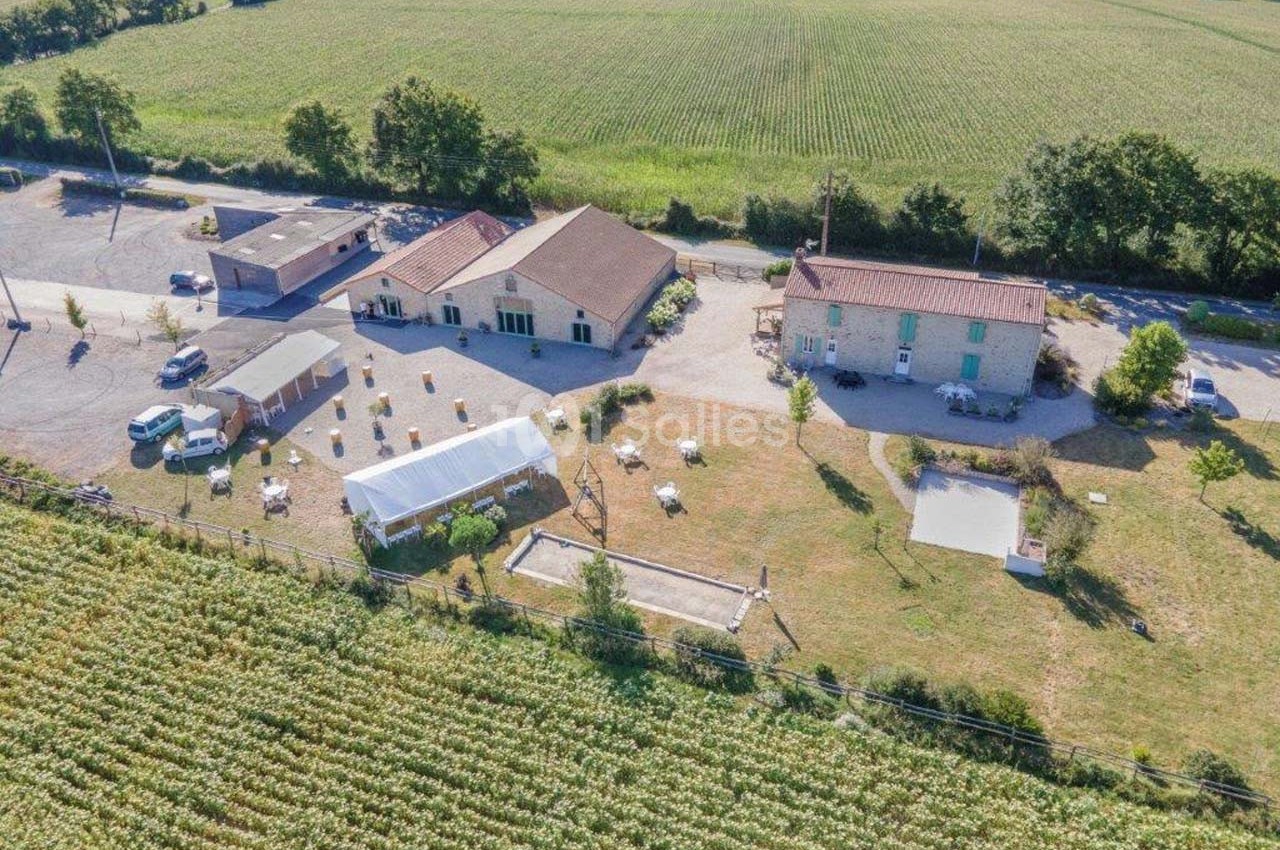 Vue aérienne d'un domaine rural avec bâtiments, serre, espace aménagé et champs environnants.