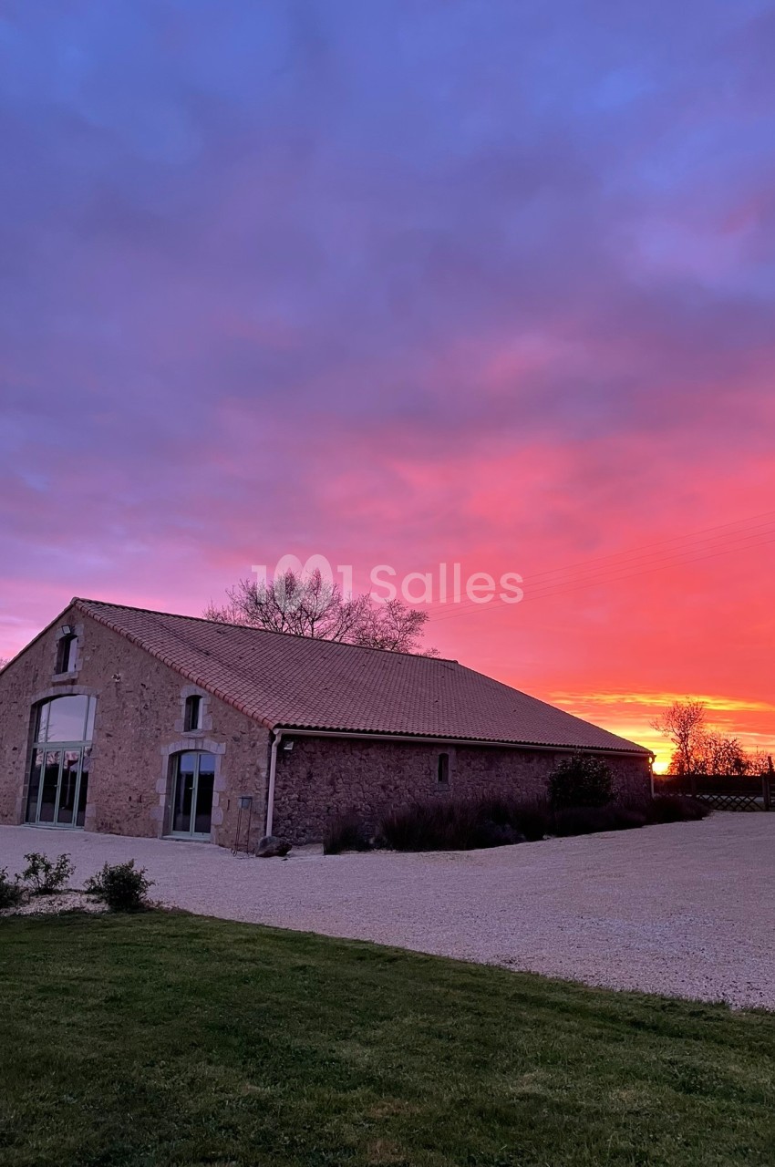 Bâtiment en pierre avec toit en tuiles, éclairé par un coucher de soleil aux teintes roses et violettes.