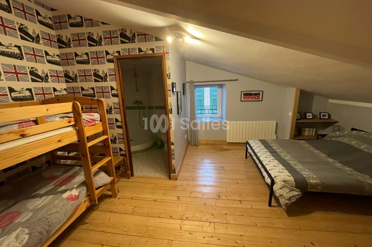 Chambre mansardée avec lits superposés, lit double, parquet en bois, salle d'eau attenante et décoration murale britannique.