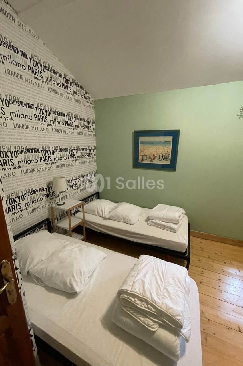 Deux lits simples avec draps blancs dans une chambre au sol en bois, décorée d'un mur avec des noms de villes.
