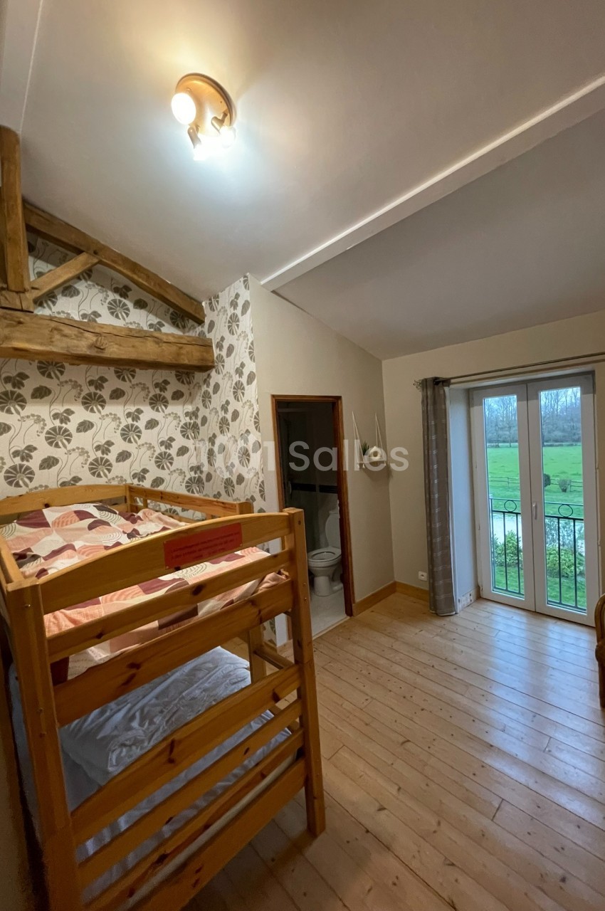 Chambre avec lits superposés en bois, parquet, papier peint floral, accès à une salle de bain et vue sur un jardin.