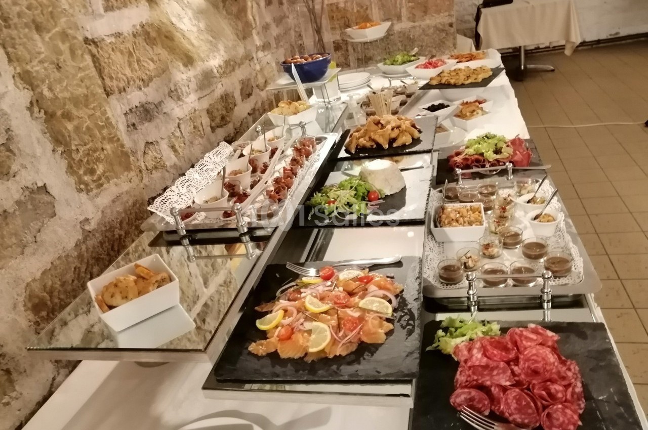 Buffet varié avec charcuterie, salades, plats chauds et desserts disposés sur une table contre un mur en pierre.