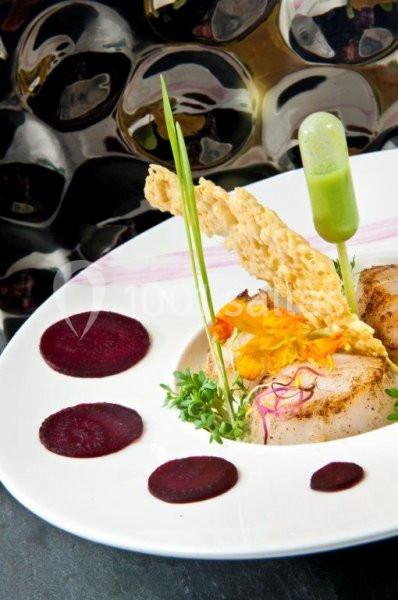 Assiette gastronomique avec viande, purée, tranches de betterave, décorations florales et pipette de sauce verte.