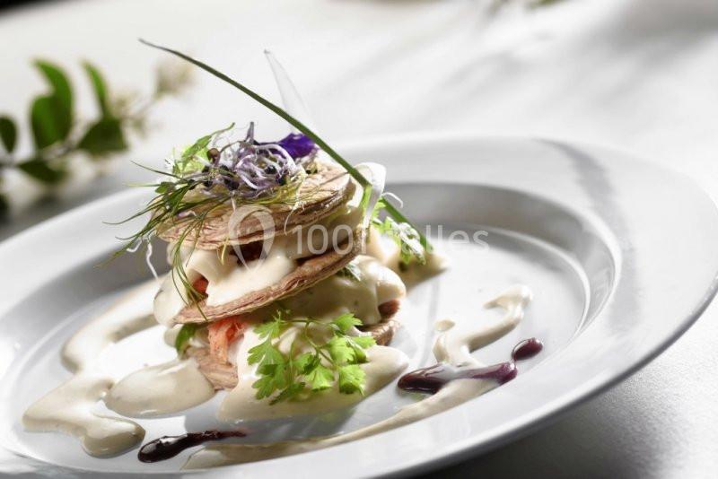 Assiette gastronomique avec un millefeuille salé garni de légumes, herbes fraîches et sauce crémeuse.