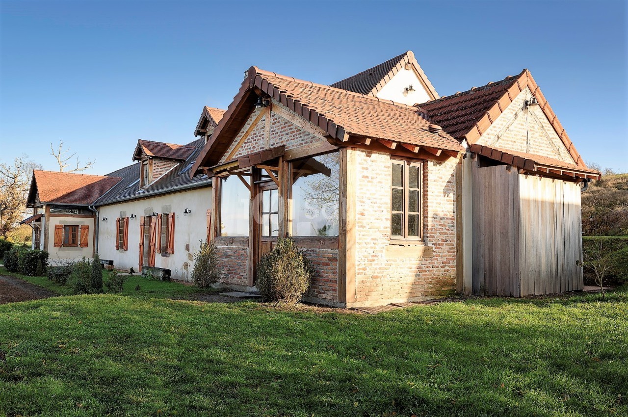 Maison en briques et bois avec toit en tuiles, entourée de pelouse et située dans un cadre rural.