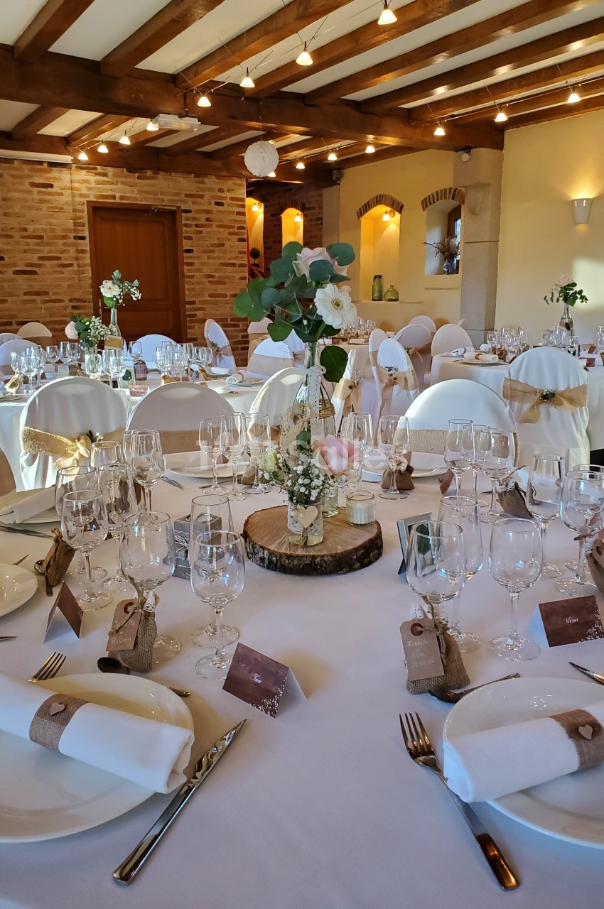 Salle de réception décorée avec des tables rondes élégantes, nappes blanches, fleurs et vaisselle raffinée.