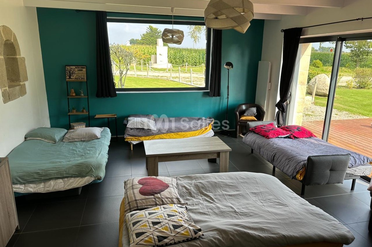 Chambre spacieuse avec quatre lits, grande fenêtre donnant sur un jardin, décor moderne et lumineux.