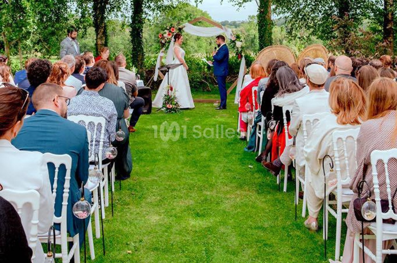 Cérémonie de mariage en plein air, avec des invités assis et un couple échangeant leurs vœux devant un décor floral.