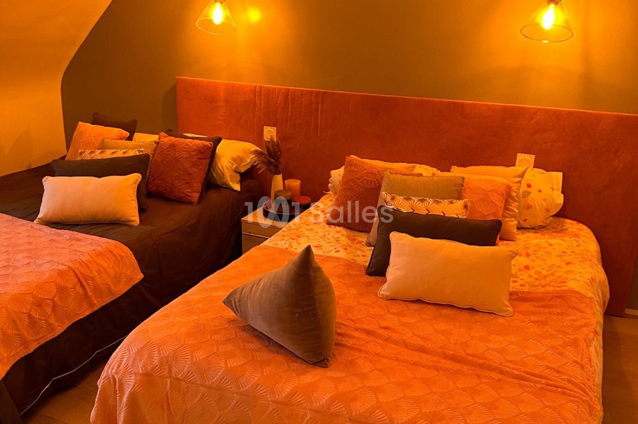 Deux lits doubles avec couvre-lits orange et coussins assortis, éclairés par des appliques murales dans une chambre…