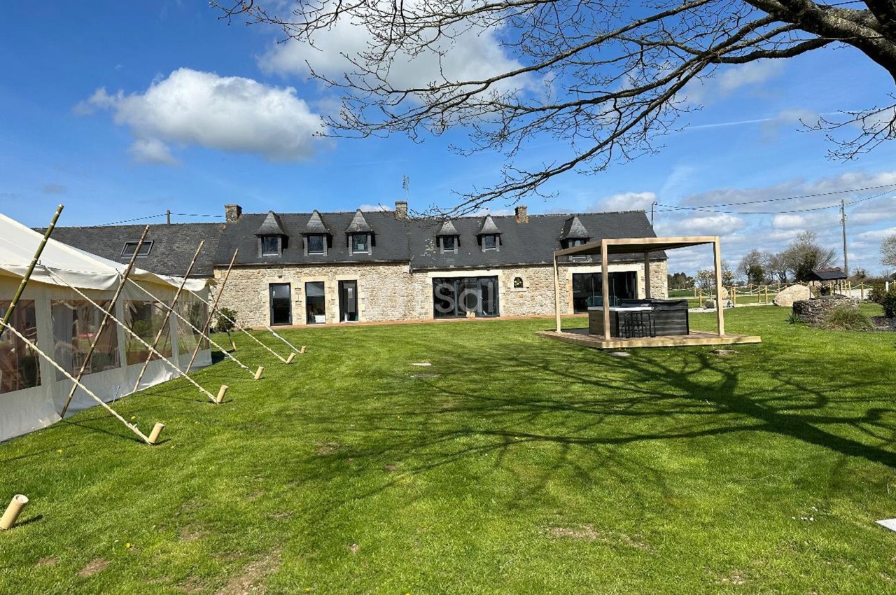 Grande maison en pierre avec toit en ardoise, entourée d'une pelouse, avec une terrasse et un jacuzzi extérieur.