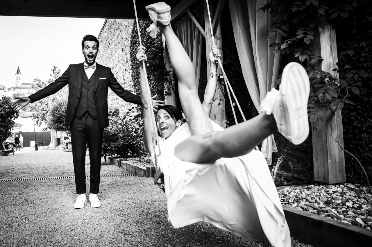 Un homme en costume surpris regarde une femme en robe blanche qui se balance joyeusement sur une balançoire.